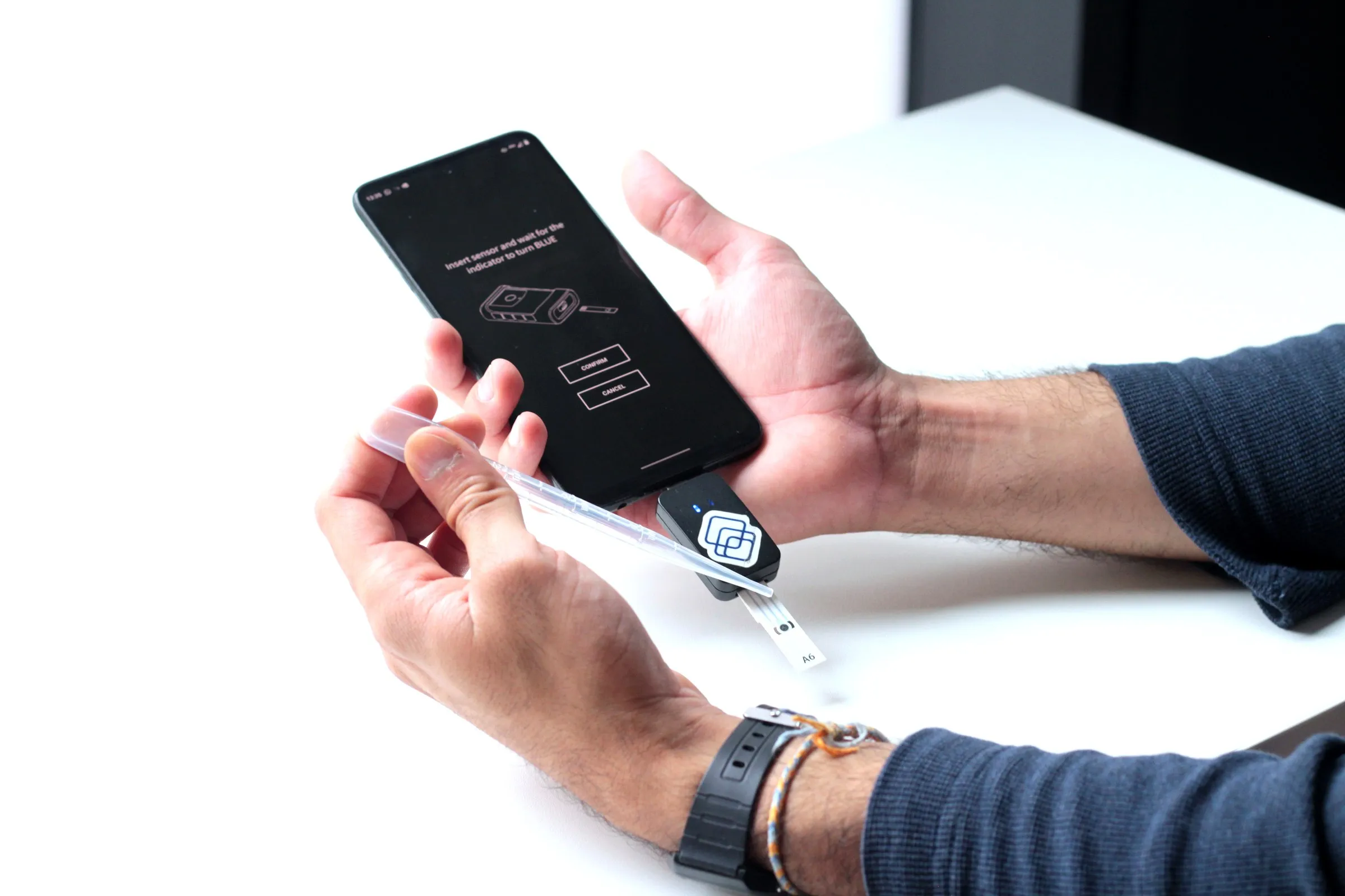 Hands inserting a Segura sensor strip into the reader, with the mobile app visible